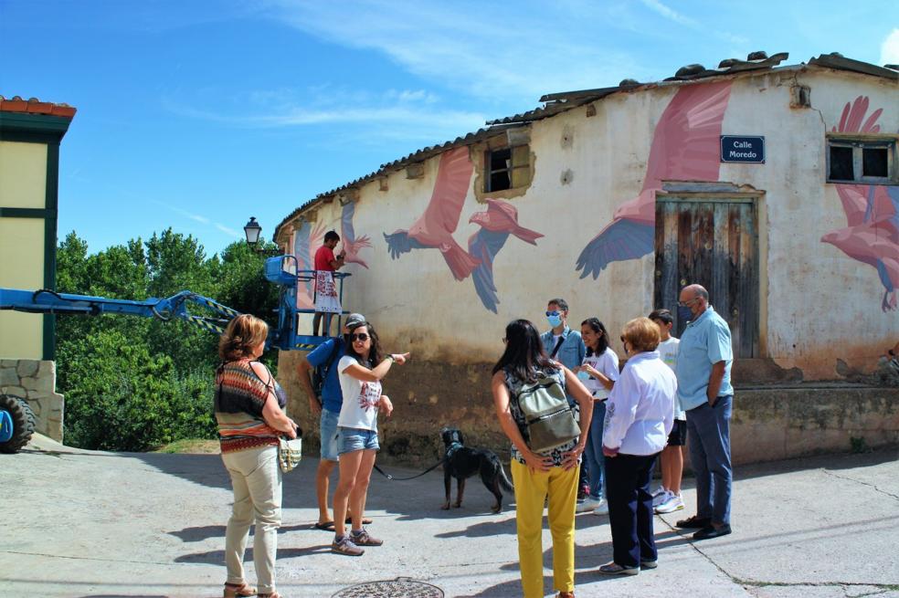 Taquen. El artista da los últimos retoques a su mural, mientras un grupo de visitantes observa su pintura. 