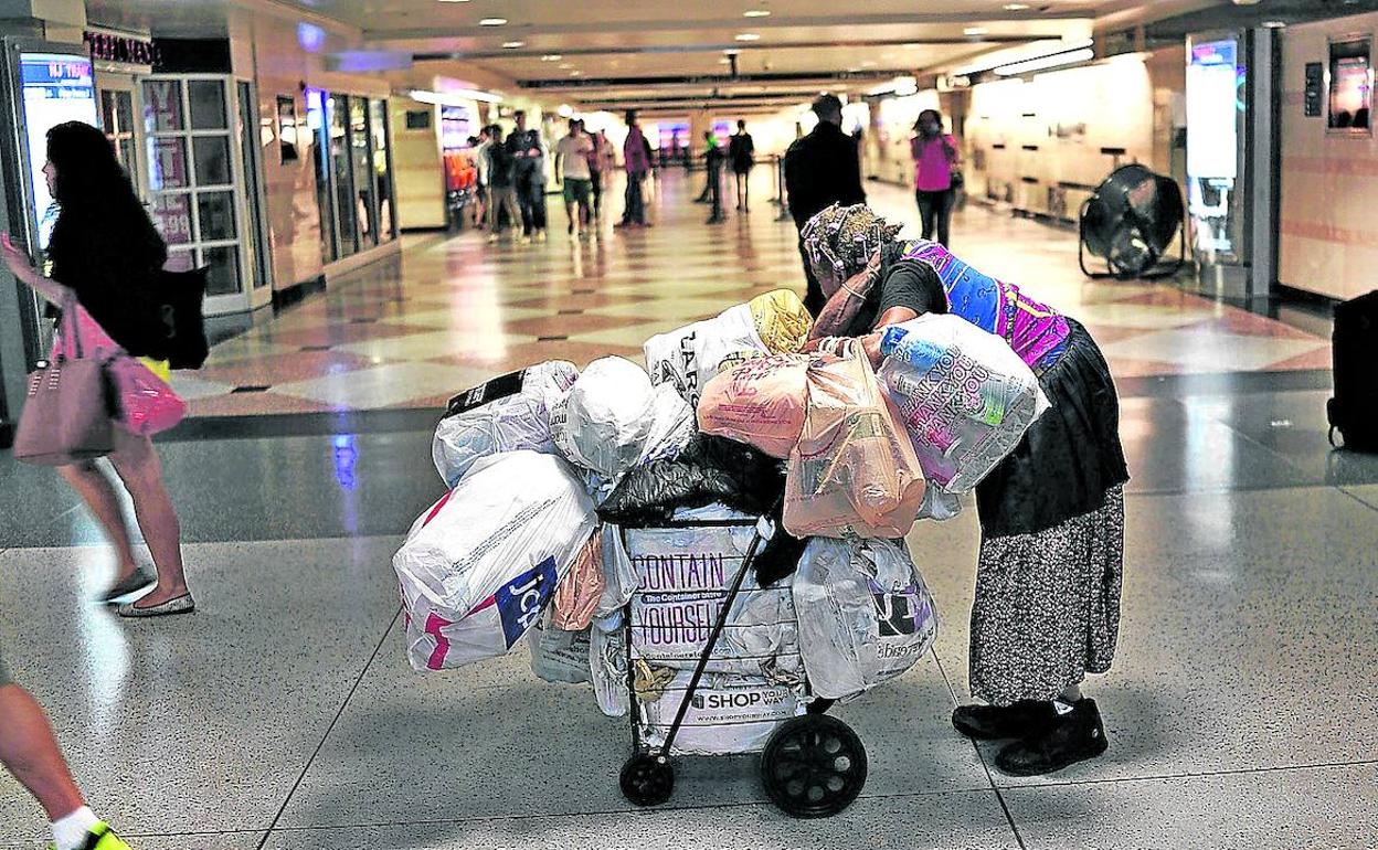 Una sintecho camina empujando un carro con sus pertenencias por los pasillos de una estación de Manhattan.