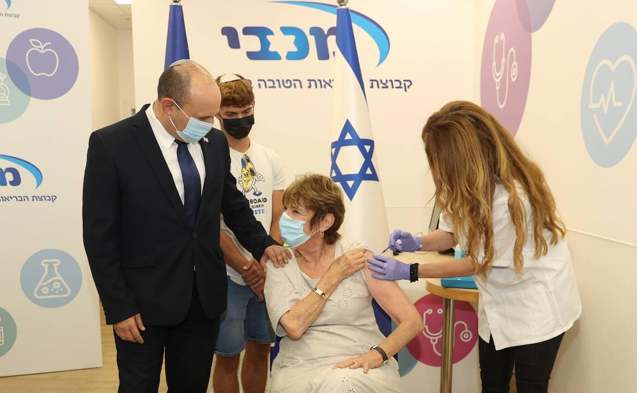 El primer ministro israelí, Naftali Bennet, acompaña a su madre mientras le aplican la tercera dosis de la vacuna contra el coronavirus.