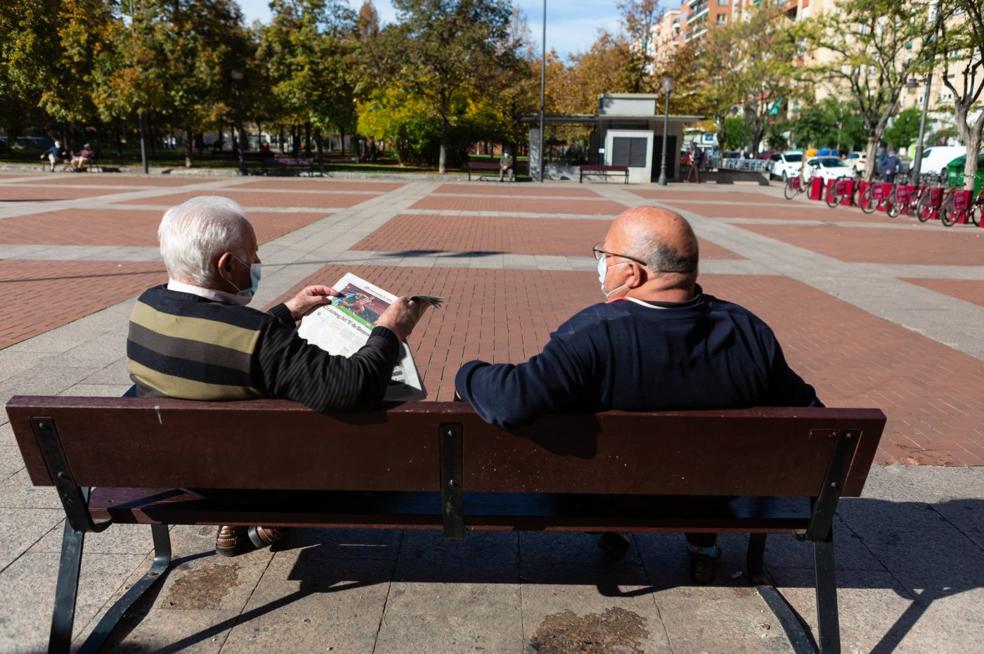 Dos hombres leen el periódico y charlan en el Paseo de la Cometa de Logroño. 