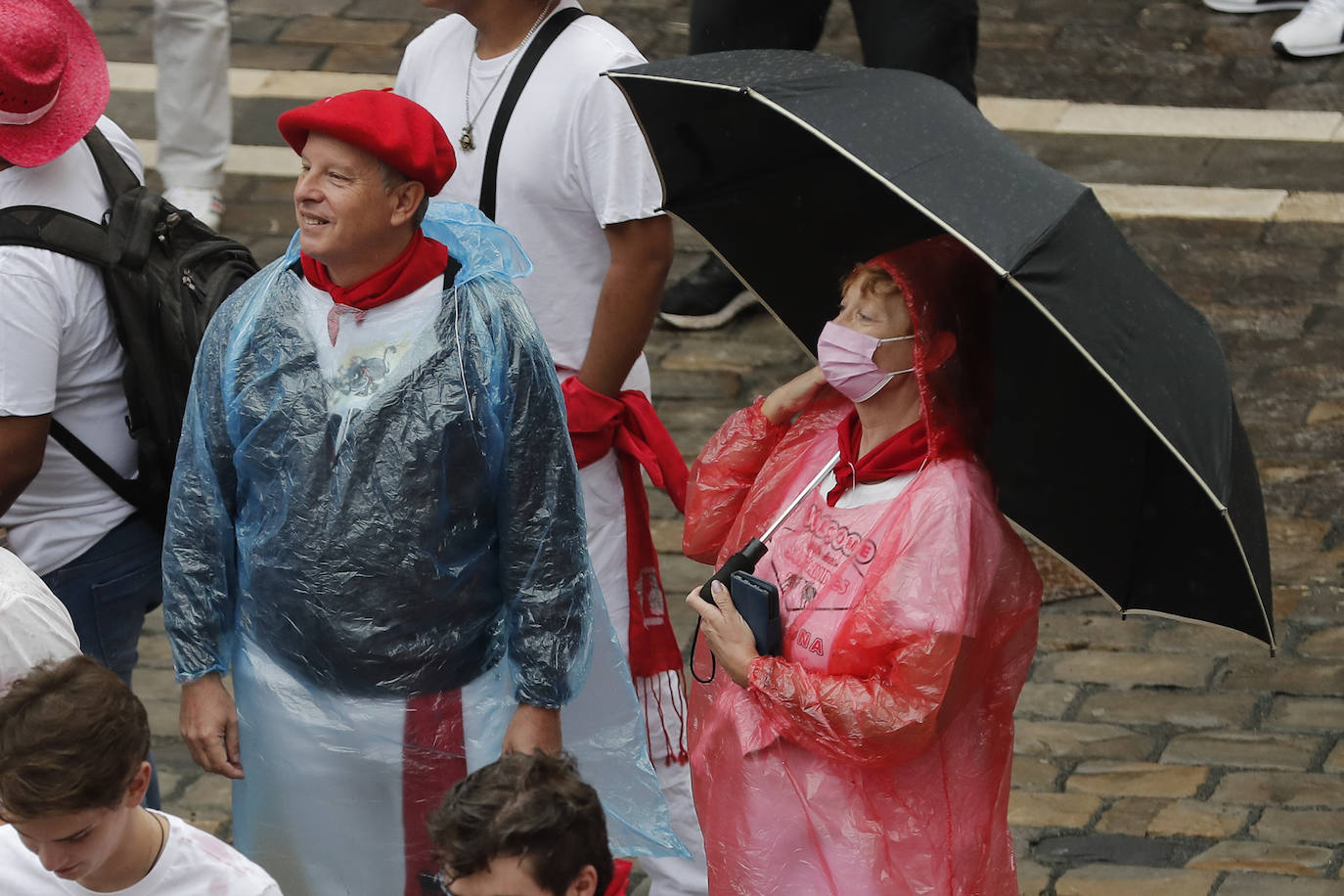 Dos personas se protegen con un paraguas y un chubasquero para evitar que la ropa se les manche del vino que corre y vuela por las calles de Pamplona. 