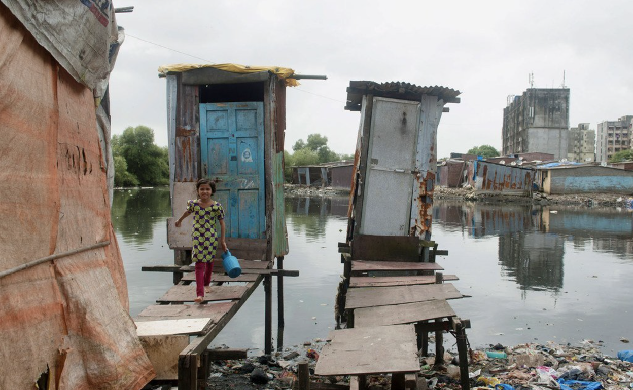 Una niña sale de un retrete hecho sobre pilares de madera, donde los residuos se vierten directamente en una fuente de agua abierta en Mumbai, India.