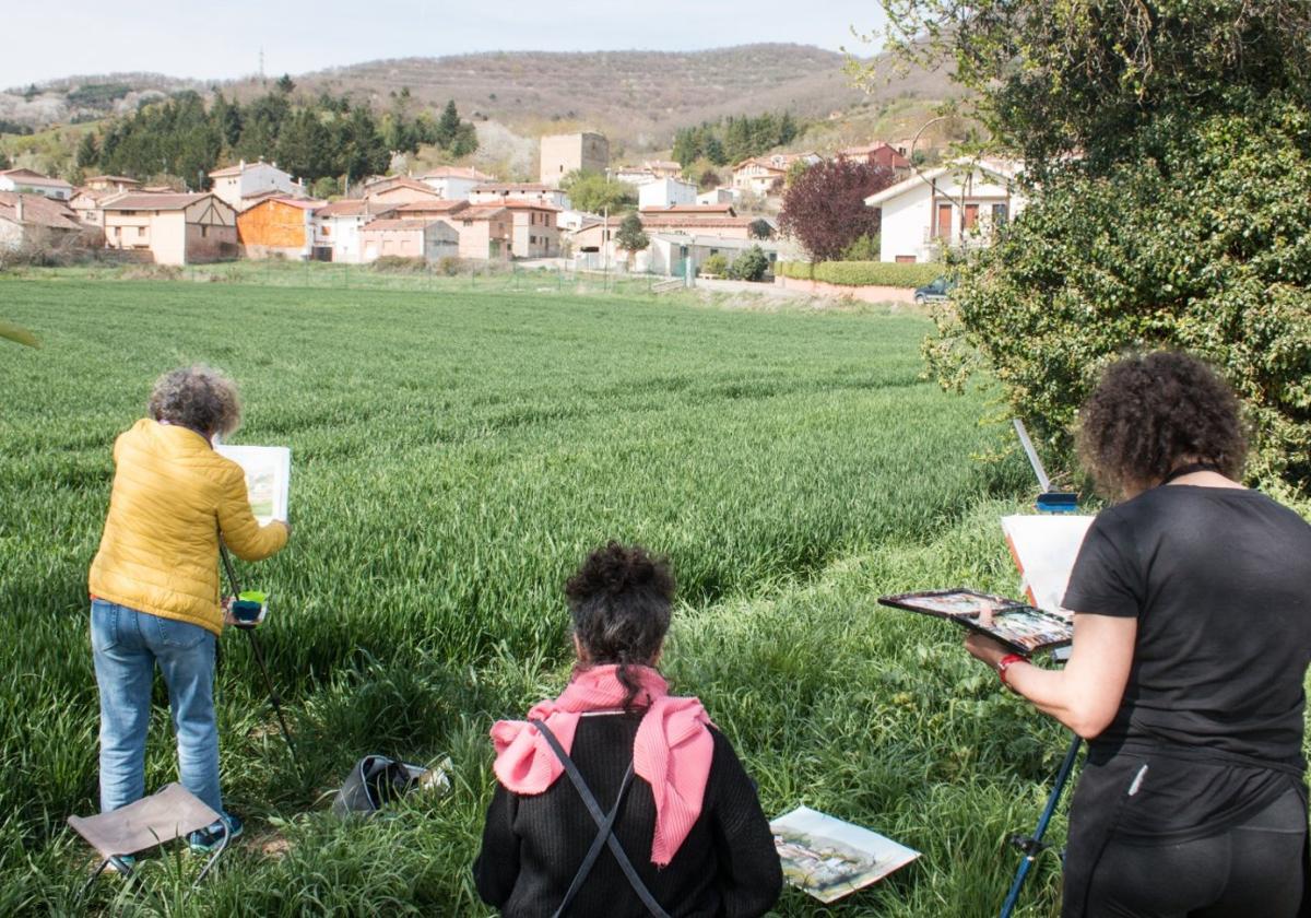 Tres de las pintoras, en un campo reflejando una vista del pueblo.