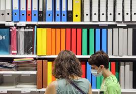 Una madre y su hijo compran material escolar en una papelería.