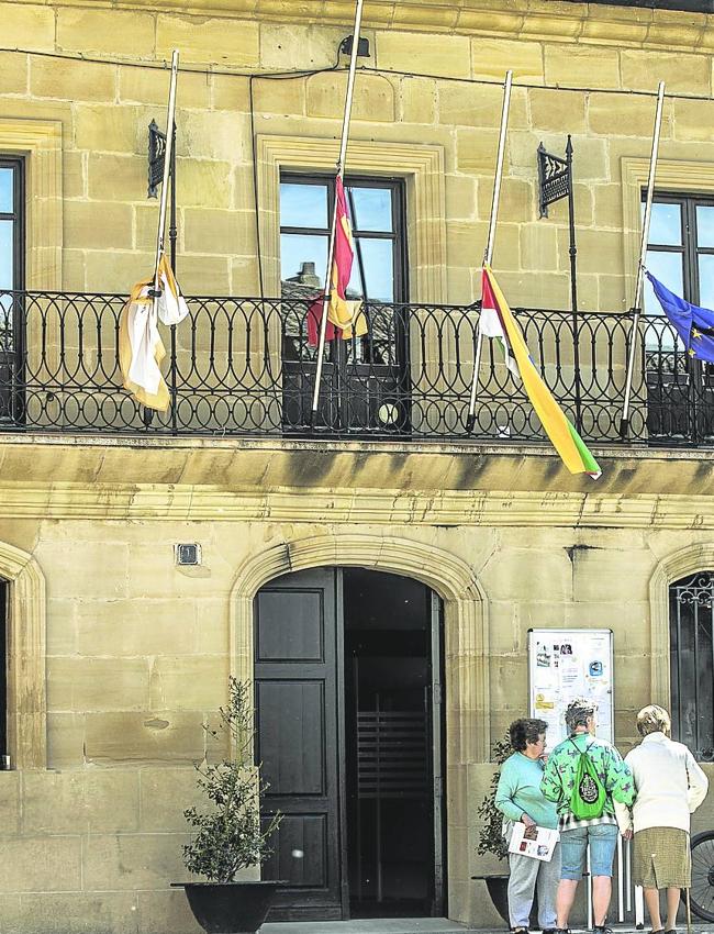 Tres mujeres charlas bajo las banderas a media asta del ayuntamiento de Cuzcurrita.