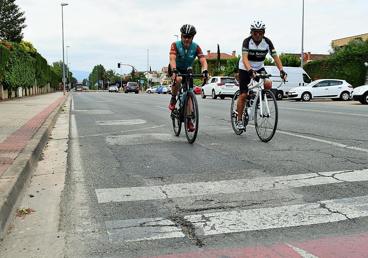 Un par de ciclistas circulan por avenida de Madrid y se acercan a un deteriorado paso de peatones.