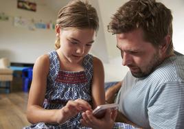 Padre e hija usando un teléfono móvil.