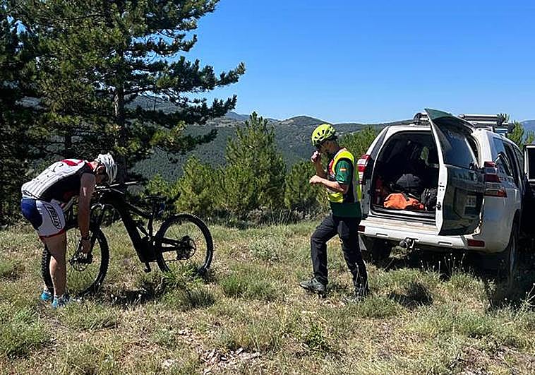 El ciclista inspecciona su bicicleta observado por un guardia civil.