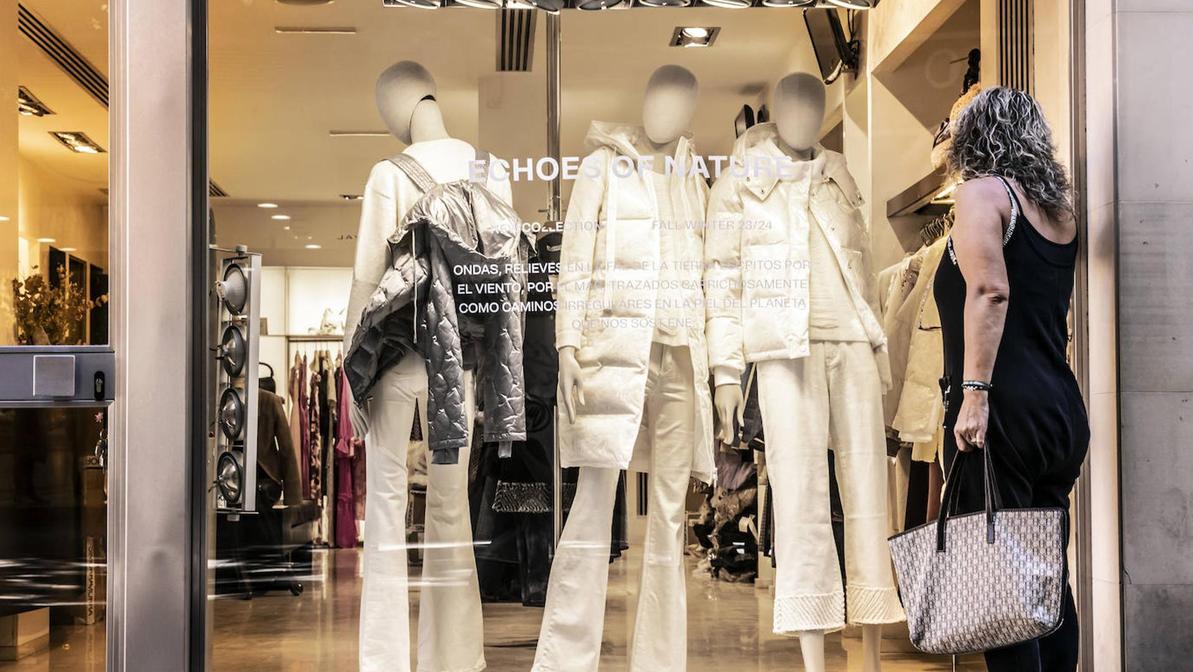 Una mujer con indumentaria veraniega mira abrigos en el escaparate de un comercio logroñés.