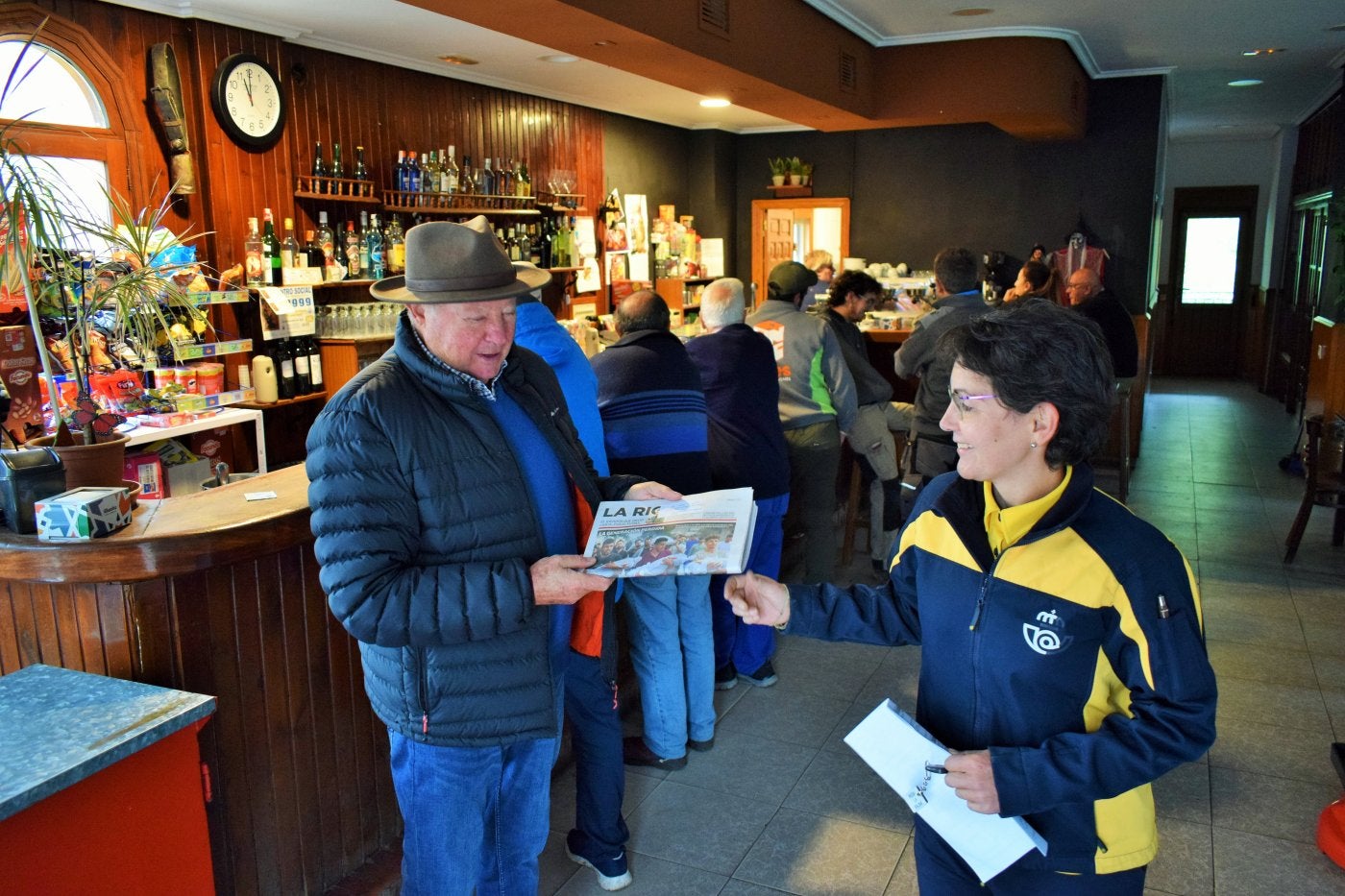 La cartera del Camero Viejo, Raquel Sáenz, entrega el periódico del día anterior al concejal de San Román, Pedro Royo, en la mañana de ayer en el bar Centro Social.