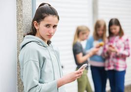 Una menor con un teléfono móvil cerca de sus amigas.