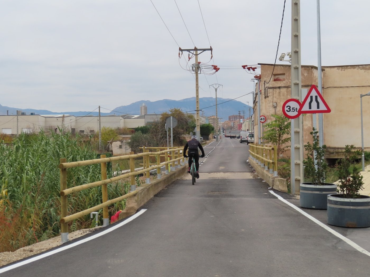 Un ciclista traspasa la angosta pasarela para adentrarse en la calle industrial de Renocal, con el casco urbano de fondo. 