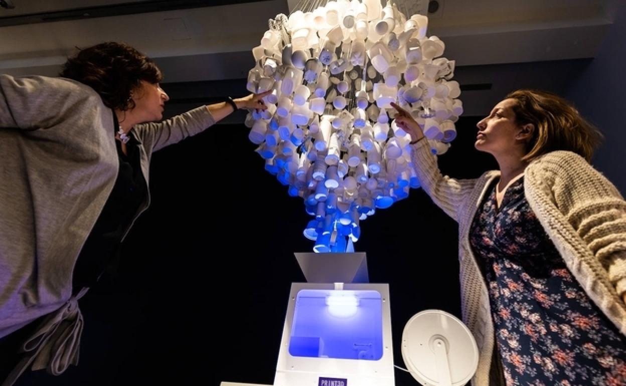 Dos mujeres tocan una trituradora para reciclaje en la exposición 'PRINT3D. Reimprimir la realidad' de CaixaForum Madrid.