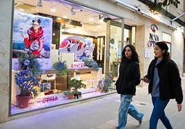Dos jóvenes pasan por delante de un original escaparate navideño, en una óptica de Achútegui de Blas.