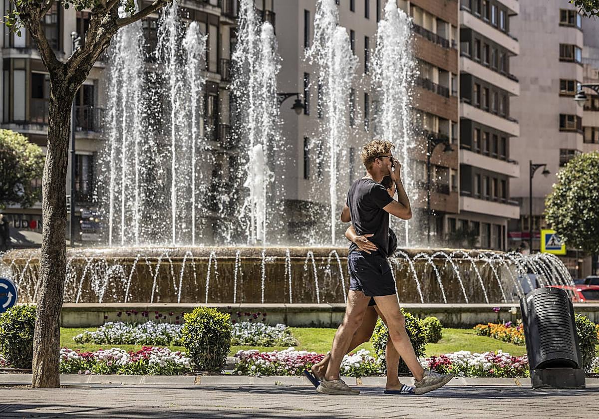Dos jóvenes en pantalón corto pasan frente a la fuente de Murrieta.