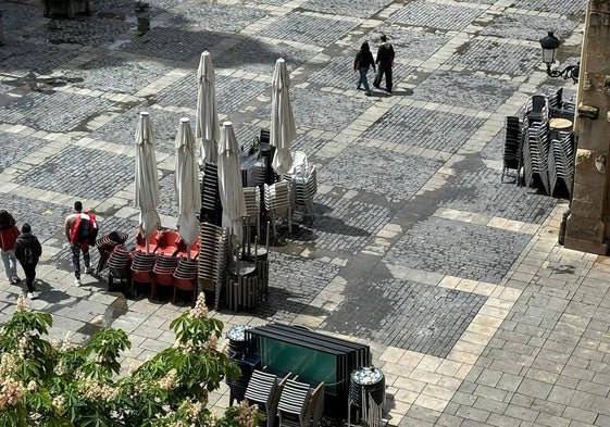 Mesas y sillas apiladas, sombrillas incluidas y diferentes colores, en la plaza del Mercado.