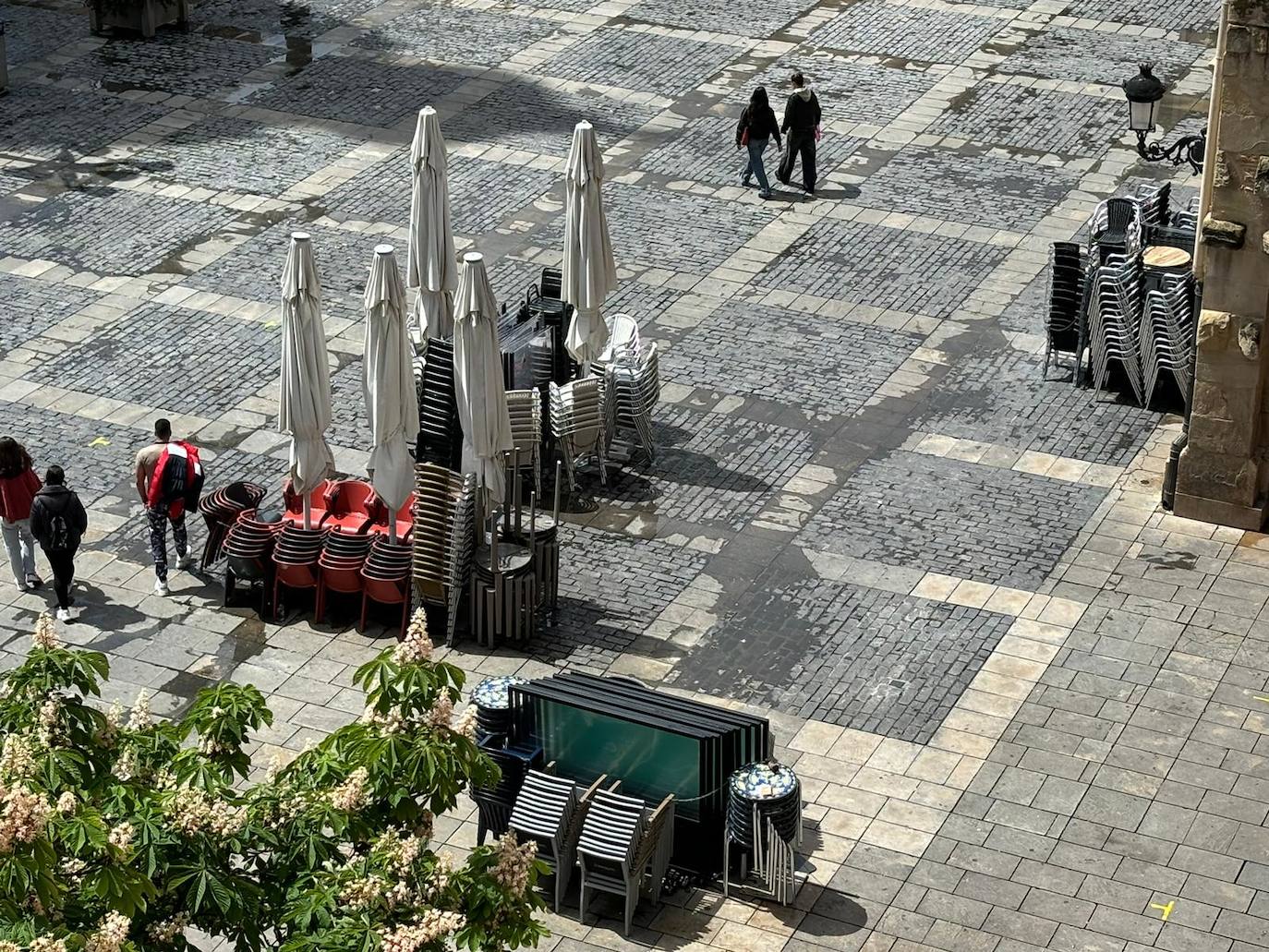 Mesas y sillas apiladas, sombrillas incluidas y diferentes colores, en la plaza del Mercado.