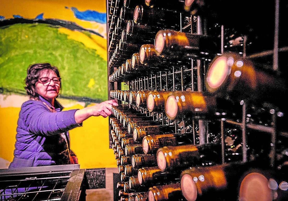 Imagen principal - Arriba, Isabel en la zona de botellas. Abajo, David atiende una visita guiada y echa vino a una copa.
