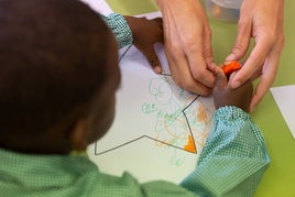 Una profesora ayuda a uno de sus alumnos a pintar un dibujo.