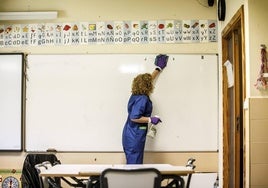 Una trabajadora de la limpieza procede a desinfectar el aula.