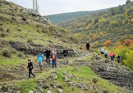 Los senderistas cruzan una zona rocosa, en medio de un paisaje otoñal incipiente.