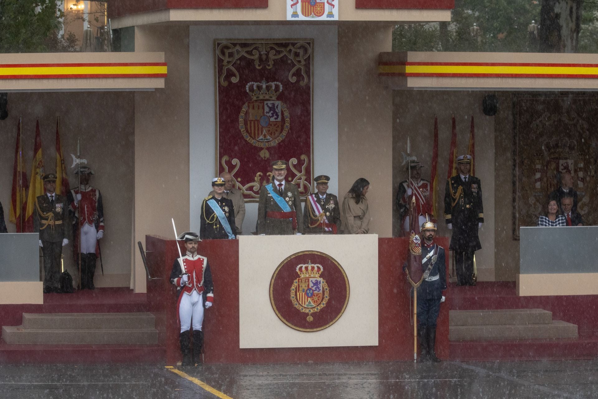La intensa lluvia obligó a acortar el desfile militar de Madrid e inpidió algunas de las exhibiciones como las aéreas. En la imagen, los Reyes y la princesa Leonor, en el palco.