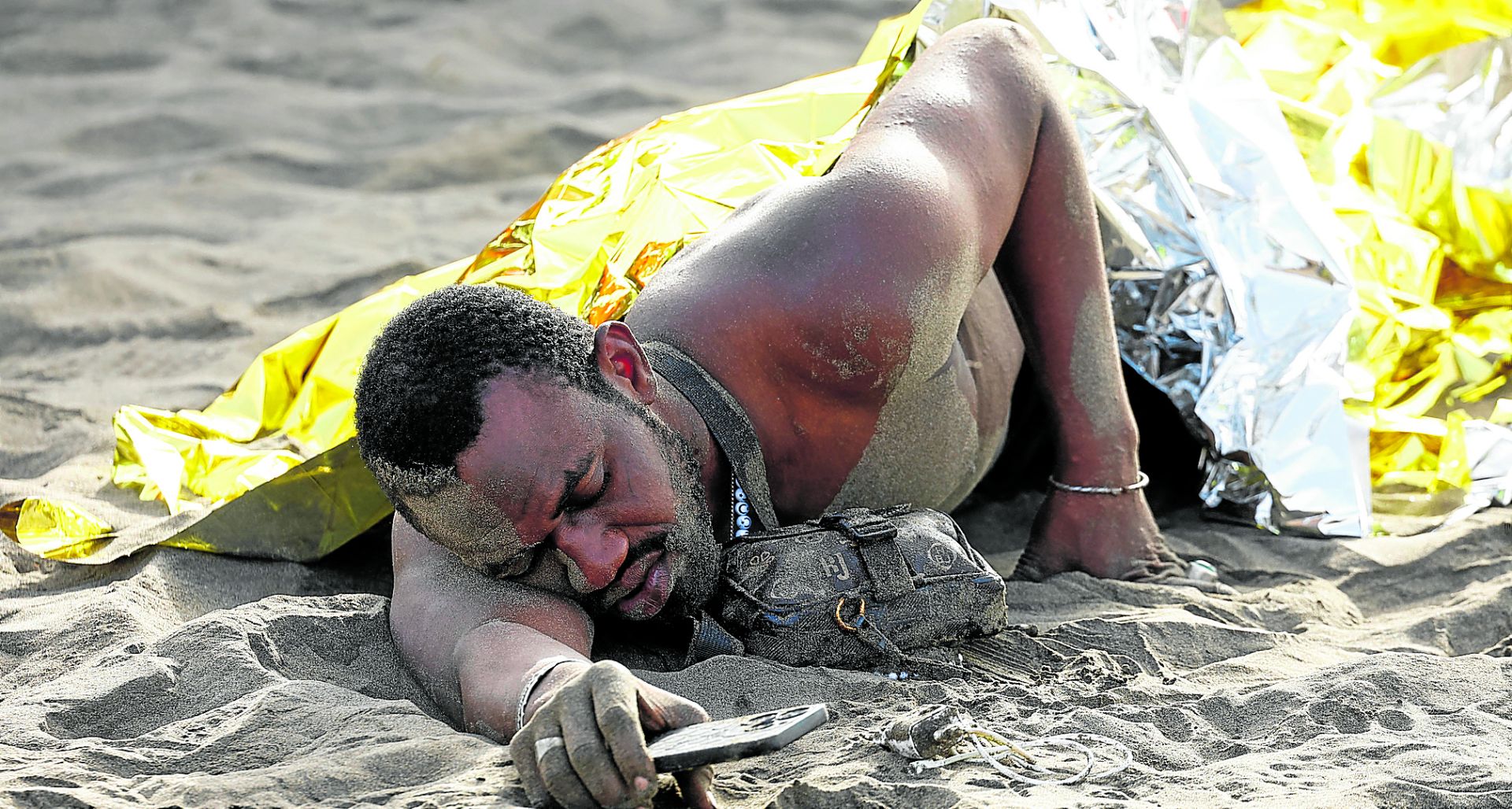 Un migrante abatido descansa en una playa canaria tras haber completado su travesía.