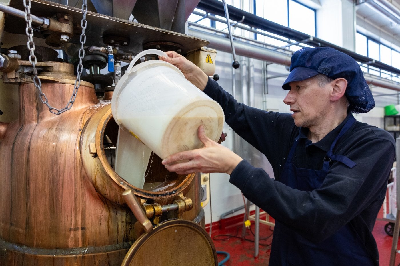 Un trabajador echa la leche en una de las ollas de cobre que cocerá la mezcla de los toffe.