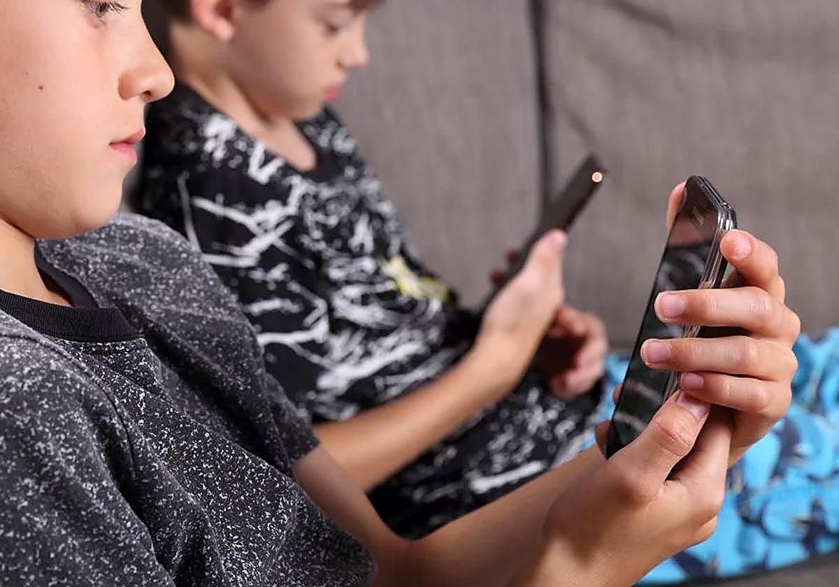Dos niños miran sus móviles.