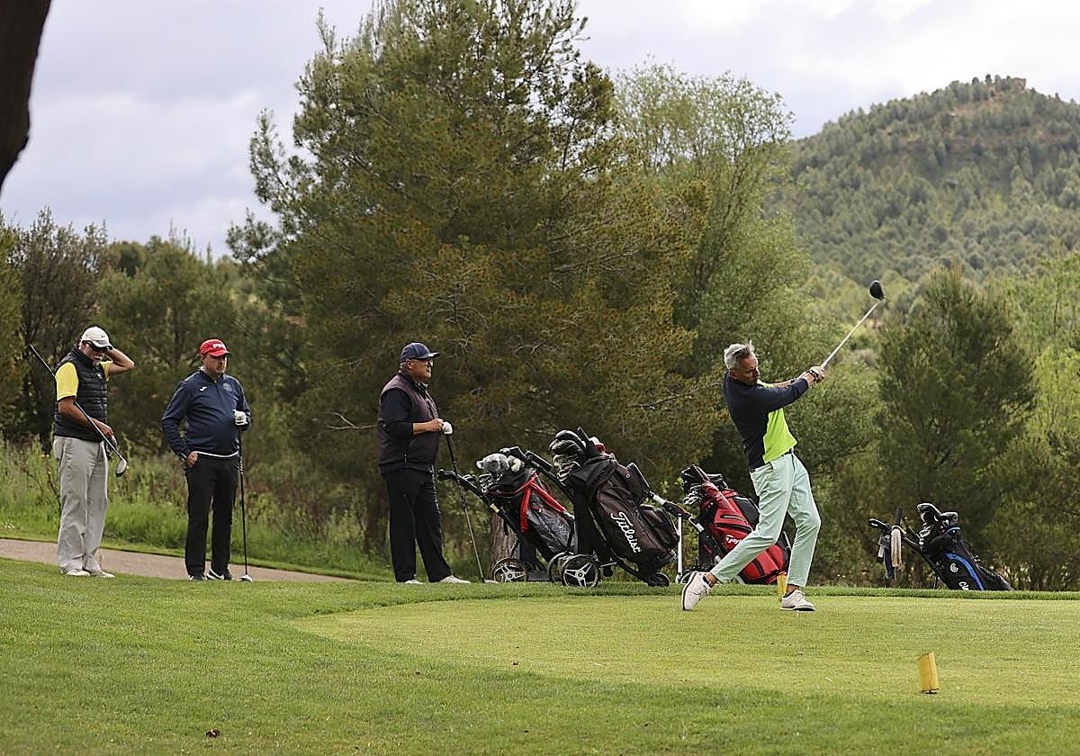 Un jugador toma la salida en un hoyo, observado por sus compañeros de partido.