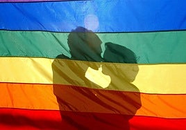 Una pareja de mujeres se besa tras la bandera LGTBI.