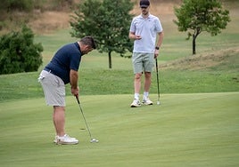 Un jugador intenta acabar el hoyo, desde el green, observado por un compañero de partido.