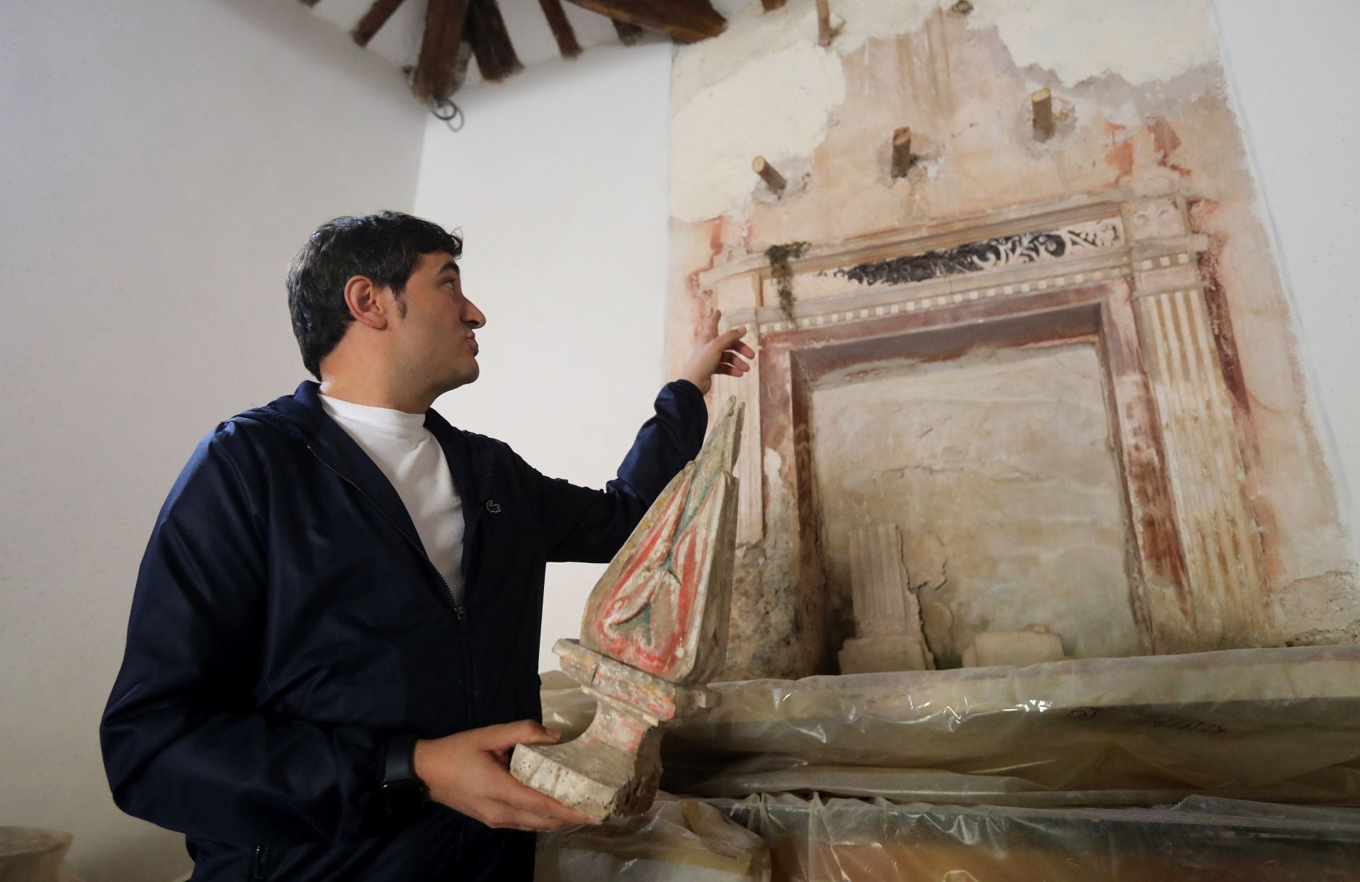 Pedro Muro, alcalde de Clavijo, señala el retablo oculto que ha sido descubierto en la ermita de San Román mientras porta en la mano una parte del retablo barroco que estaba a la vista.