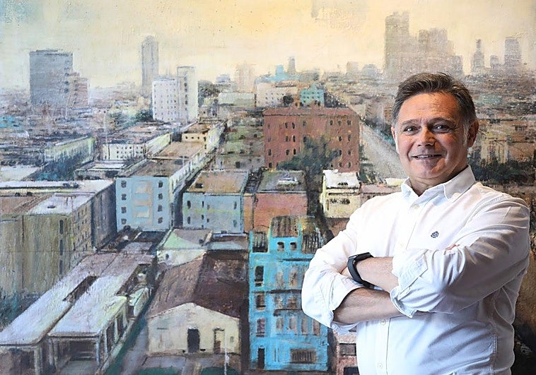 El artista Manuel Romero posa ante su pintura de La Habana.