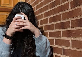 Una joven se tapa el rostro con un teléfono móvil.