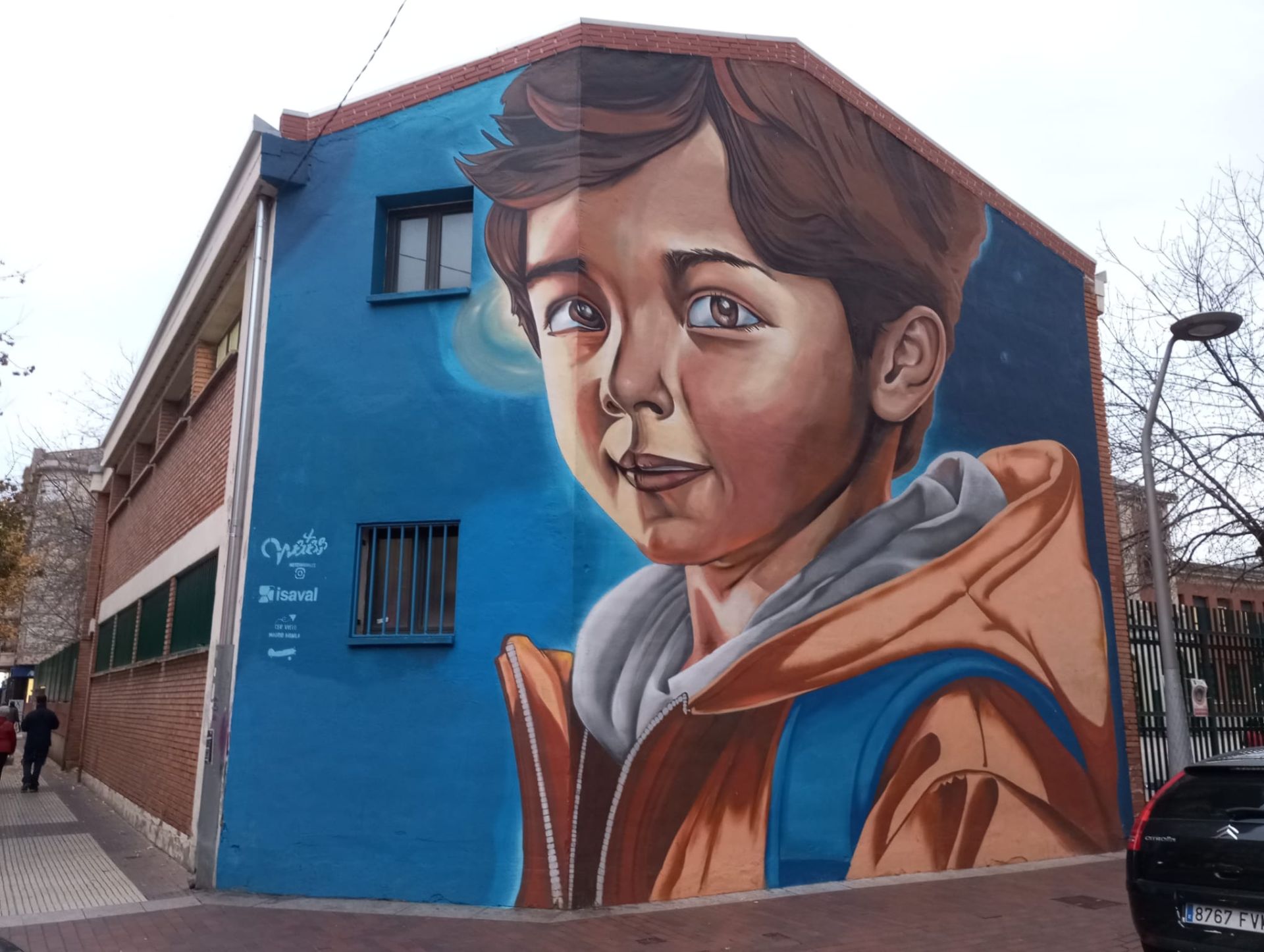 La esquina de Huesca con Gil de Gárate, con la fachada de un edificio del CEIP Vuelo Madrid Manila como lienzo, pasó de un mural de David Vicent (Deyz) en Artefacto 2014 vía espray a otro de Wetes Murales Graffiti con la colaboración de pinturas Isaval.