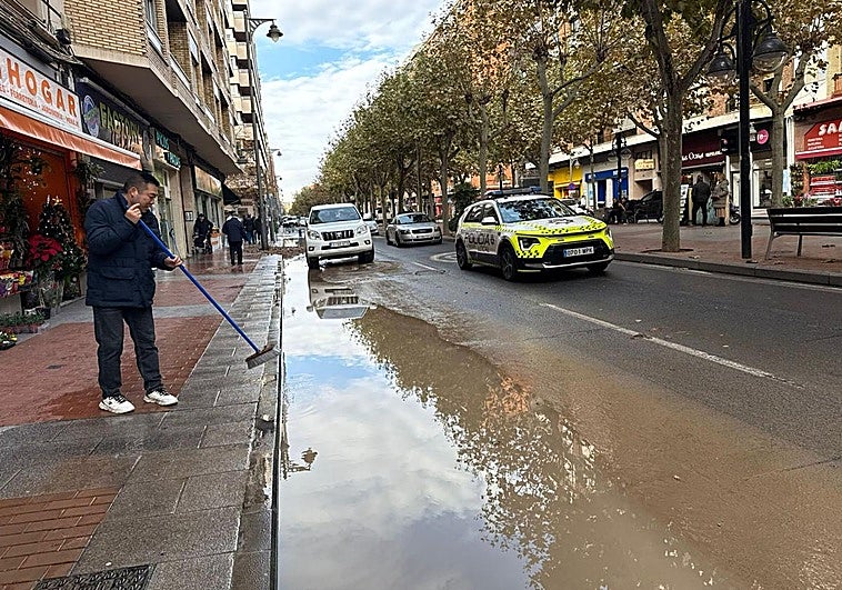 Un comerciante achica el agua de la acera junto a su tienda.