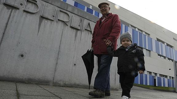 Un abuelo lleva de la mano a su nieto hacia el colegio.