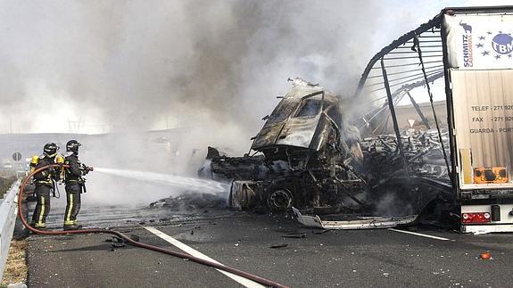 Dos bomberos intentan sofocar el fuego que se ha producido tras la colisión de los camiones.