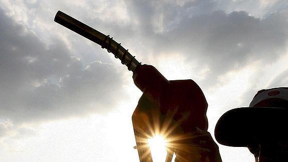 Un trabajador de una gasolinera sostiene la manguera de un surtidor.