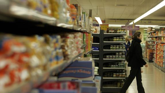 Una mujer camina entre los estantes de un supermercado.