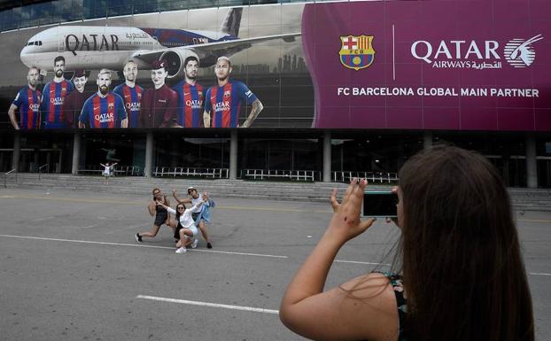 Turistas se fotografían junto a un cartel publicitario de Qatar Airways en el Camp Nou. 