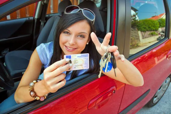 Joven y sin experiencia. Una conductora joven muestra su carnet de conducir y las llaves de su nuevo vehículo. 