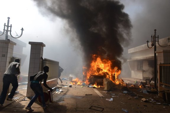 Manifestantes asaltan el Parlamento de Burkina Faso y prenden fuego a un vehículo. A la derecha, el traslado de un hombre herido en los choques de la capital con las fuerzas de seguridad mientras otro grupo de opositores lanza consignas desde los escaños vacíos de la Cámara. 