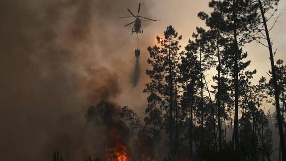 Un helicóptero vacía la carga líquida sobre unas llamas.
