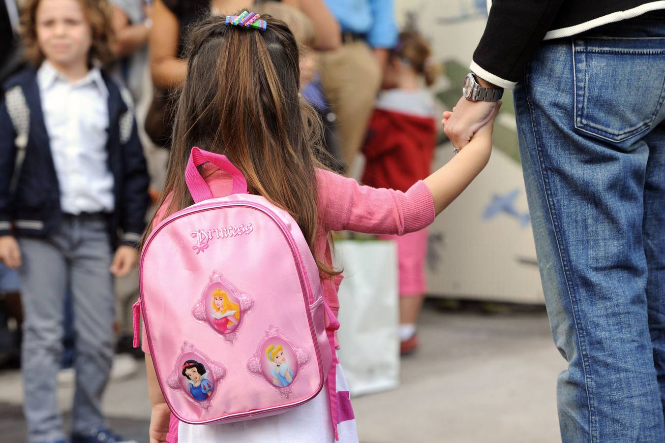 Una niña llega al colegio de la mano de su papá. 