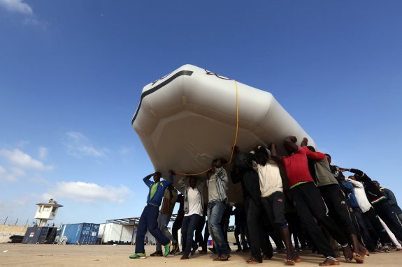 Emigrantes rescatados por guardacostas libios ayudan a trasladar una lancha en una base naval cercana a la capital, Trípoli. :: M. TURKIA / afp