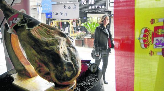 Jamón ibérico expuesto en un escaparate de una ciudad china, junto a una bandera española.