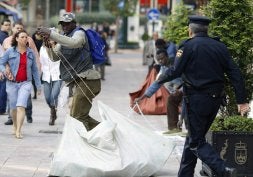 Un 'mantero' recoge sus mercancías ante la llegada de un agente de la Policía Nacional./ QUÉ