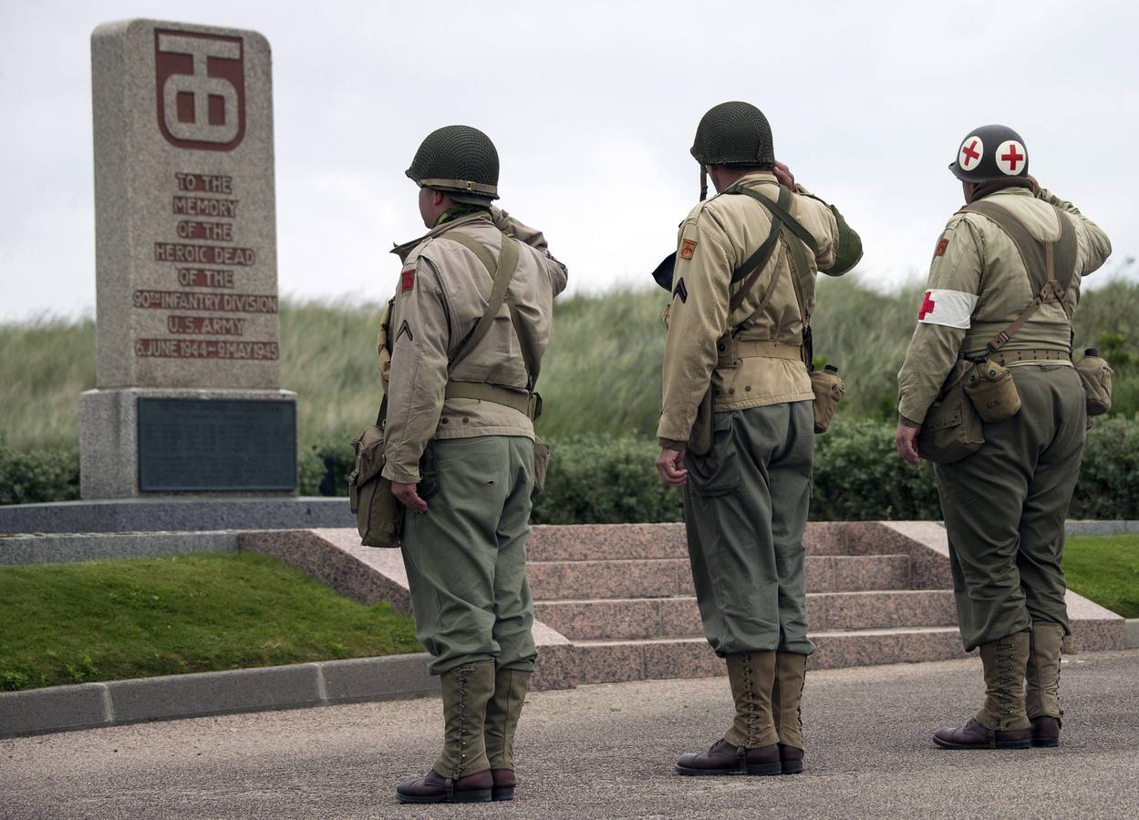 Varios entusiastas de la historia de la Segunda Guerra Mundial, vestidos con réplicas de uniformes militares de la época, saludan frente al monumento conmemorativo en la playa de Utah, cerca de Saint-Marie-Du-Mont.